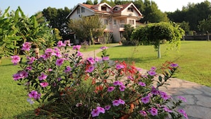 A large house with a red roof, surrounded by a well-maintained garden with pink flowers and a lawn.