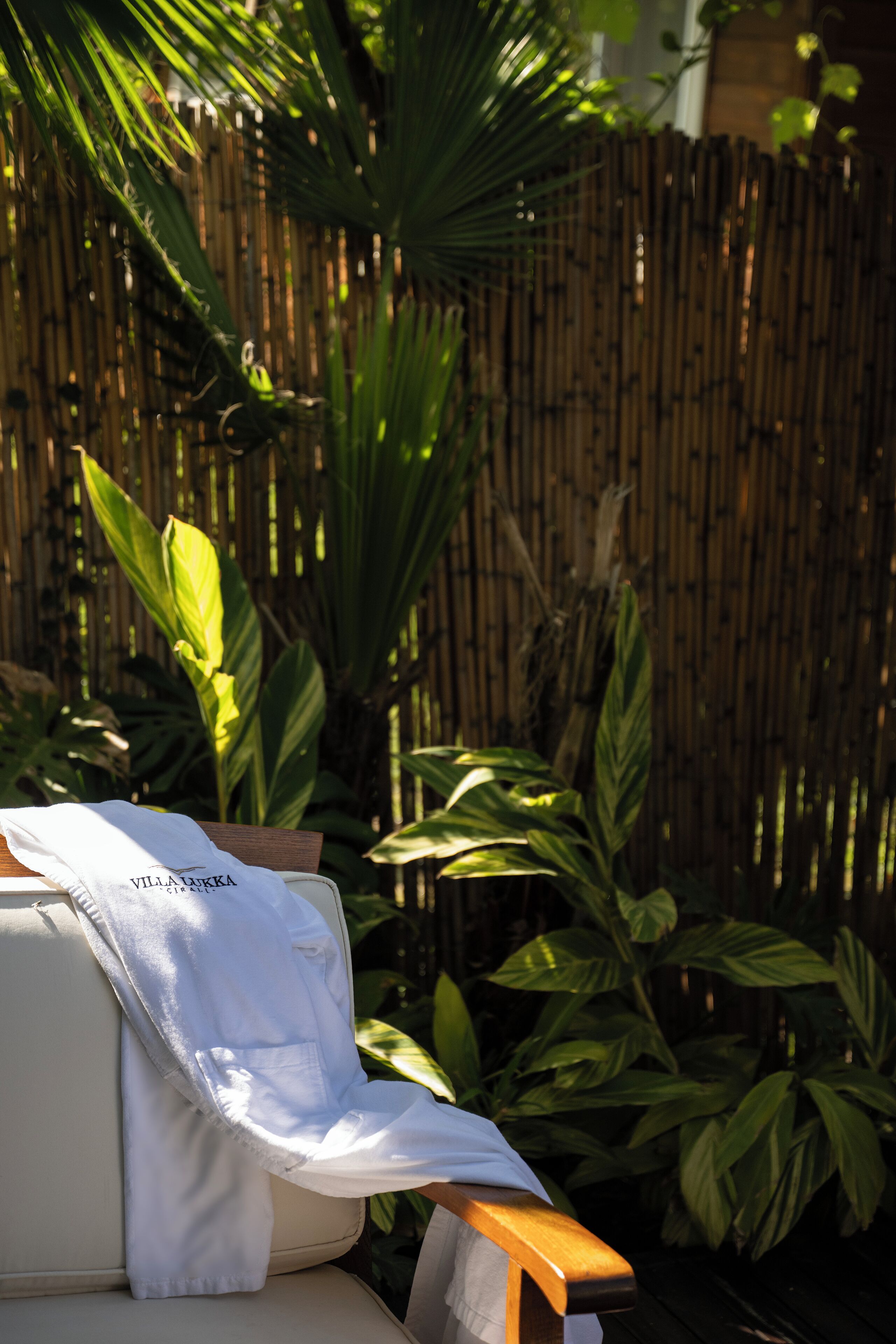 A white sofa with a white towel draped over it, positioned in front of a bamboo fence with green foliage.