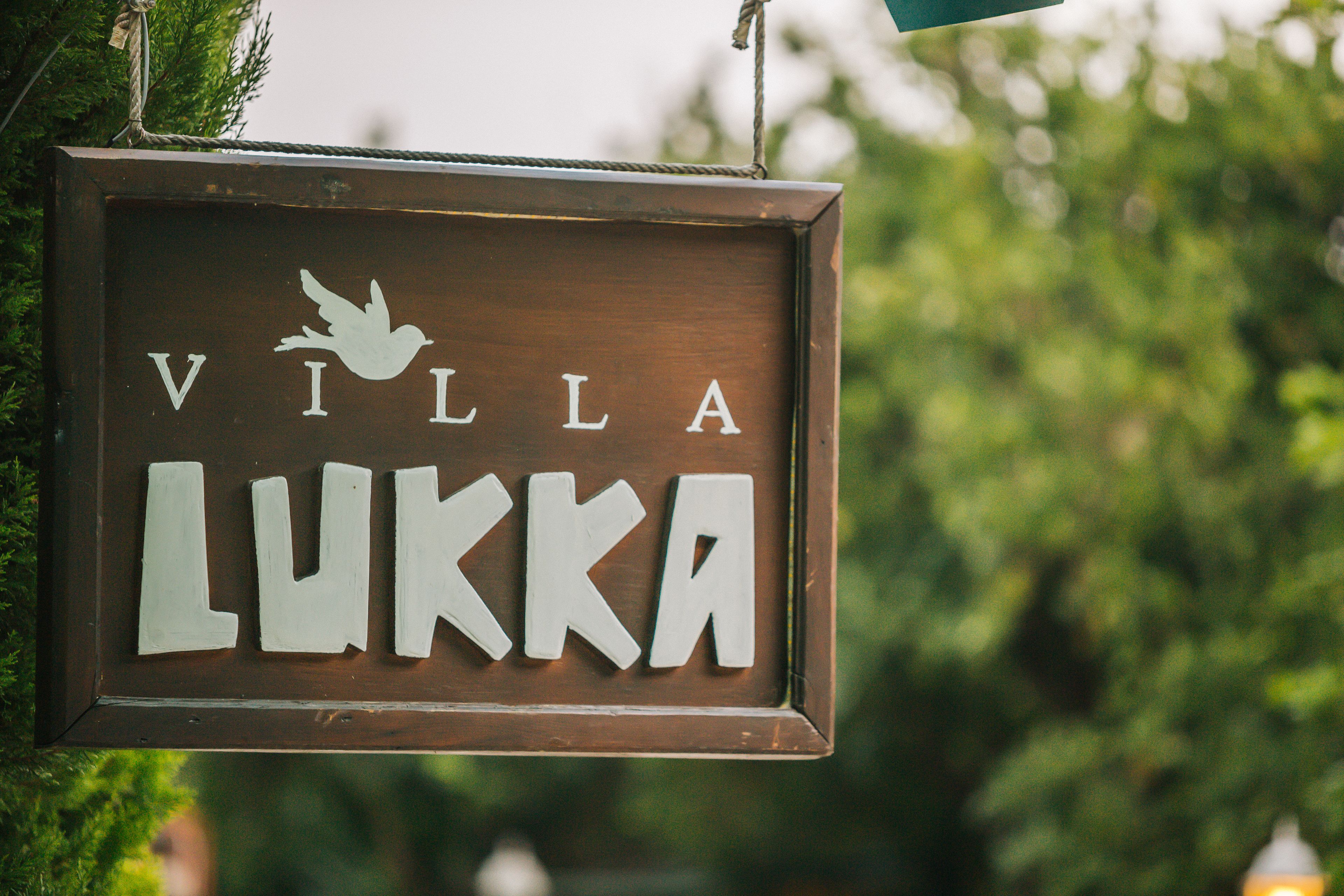 Un cartello di legno con il nome 'Villa Lukka' e un simbolo raffigurante un uccello.