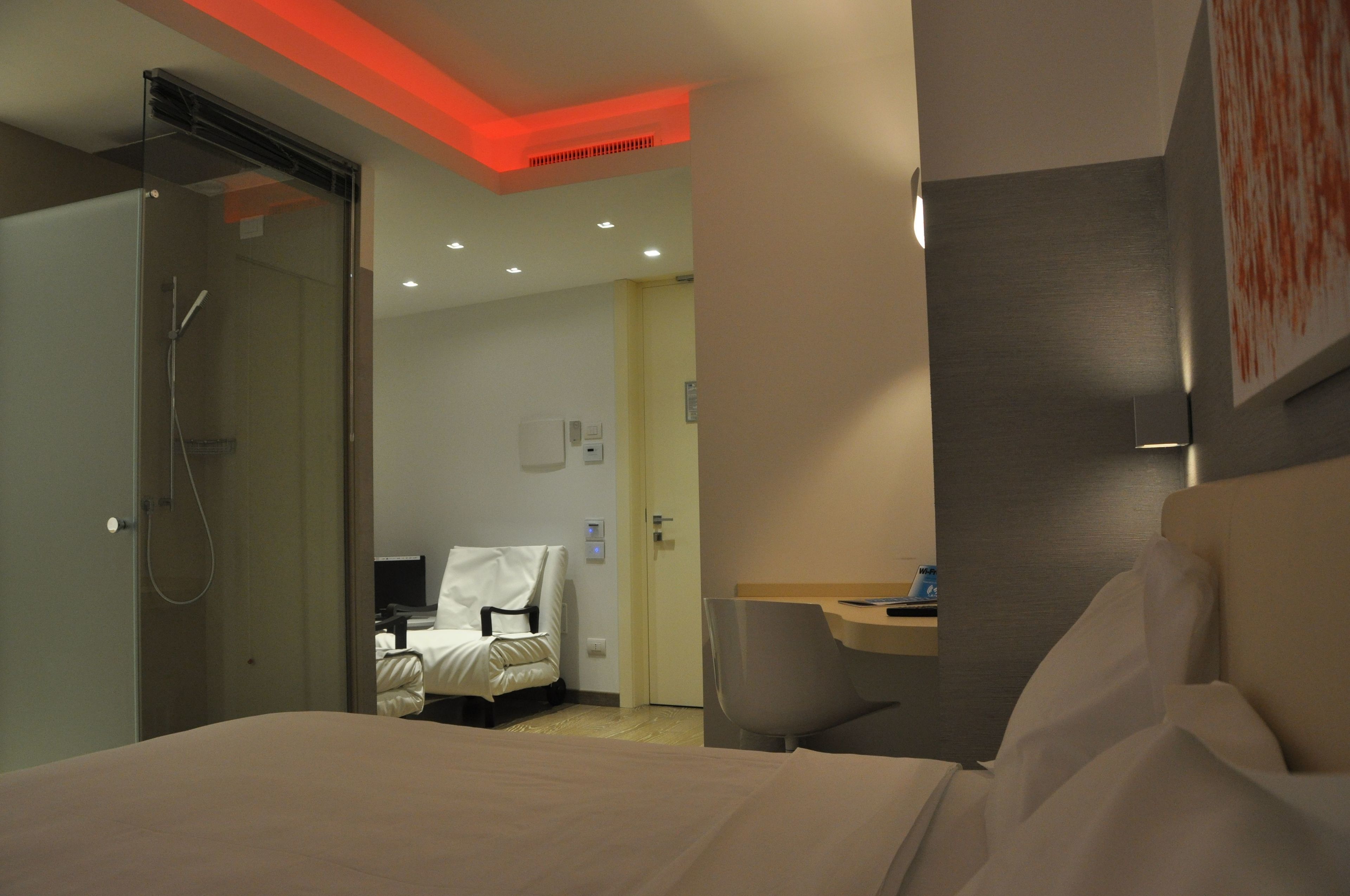 A hotel room with a bed, a desk, a chair, and a shower area.