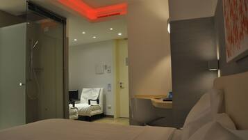 A hotel room with a bed, a desk, a chair, and a shower area.