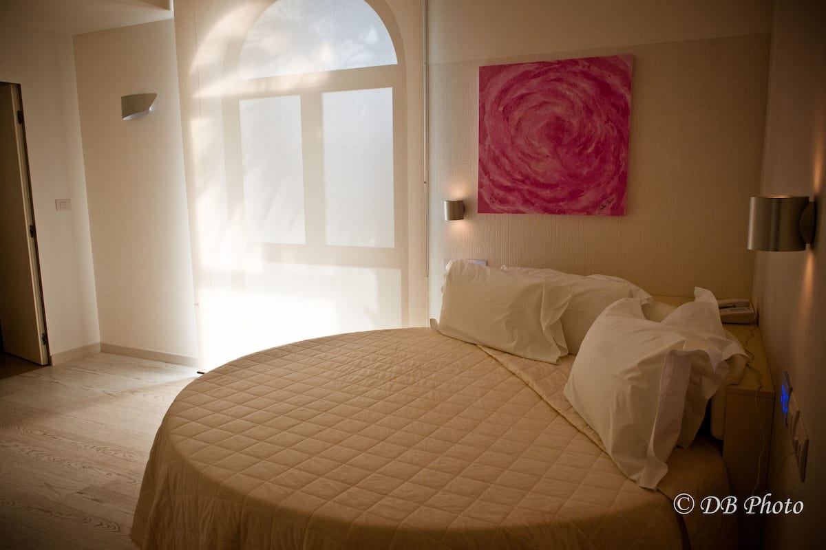 Ein Schlafzimmer mit einem großen Bett, einem Fenster mit Blick, einem rosa abstrakten Gemälde an der Wand und einer Nachttischlampe.