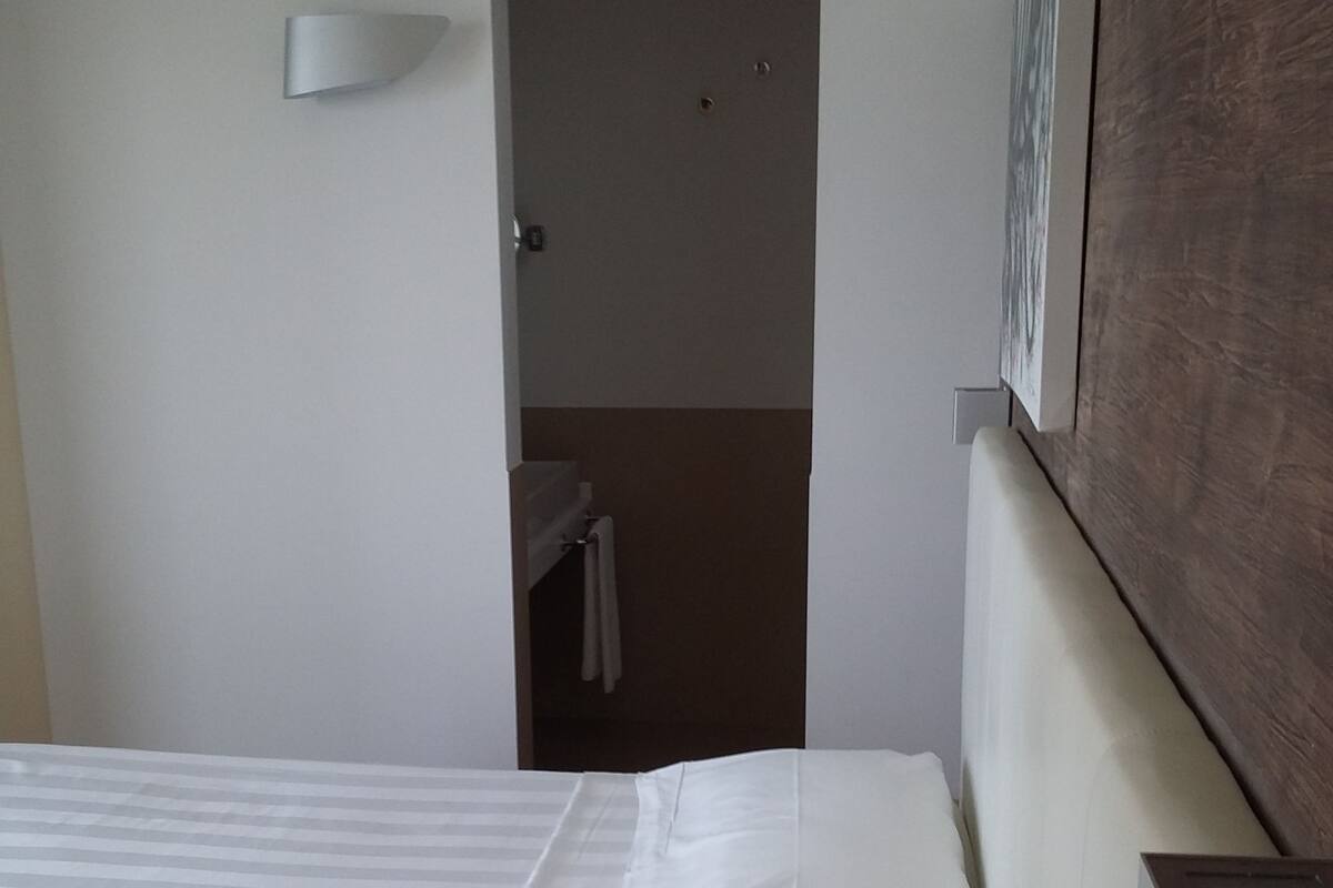 Ein Hotelzimmer mit Bett, einem Holz-Kopfteil, einer Wandleuchte und einer Tür zu einem Badezimmer.