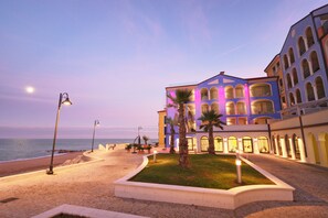 Hotel aan het strand met een goed verlichte binnentuin, palmbomen en uitzicht op de oceaan.