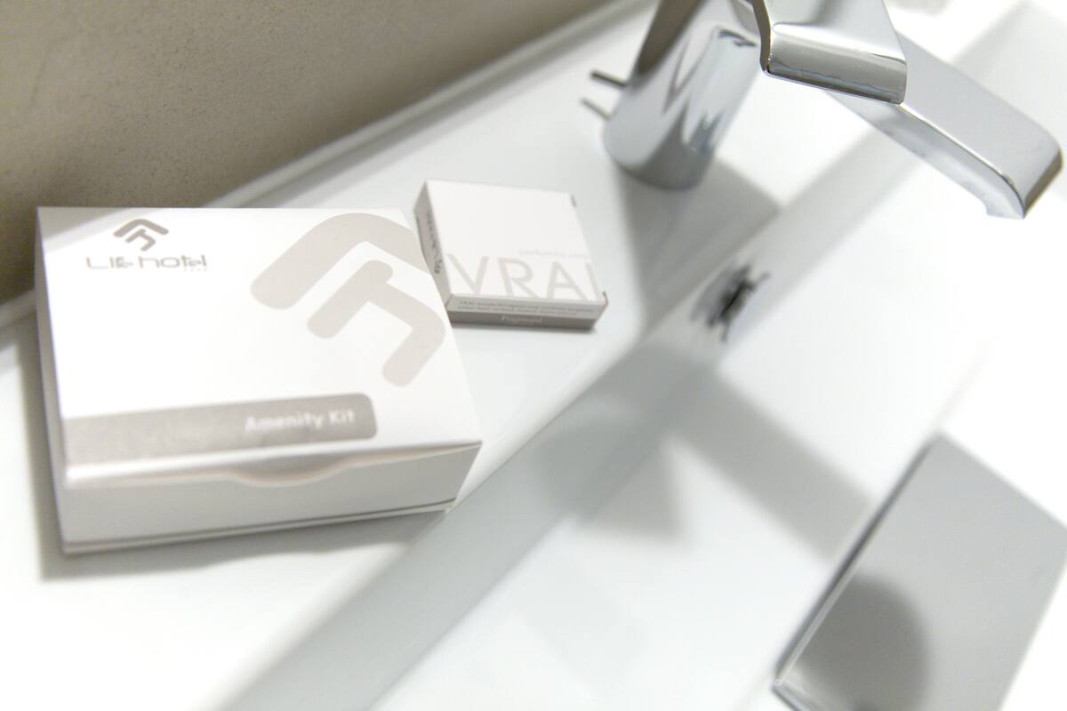 Ein Badezimmer mit einem modernen Wasserhahn und einer auf der Ablage liegenden Box mit dem Schriftzug 'VRAI'.
