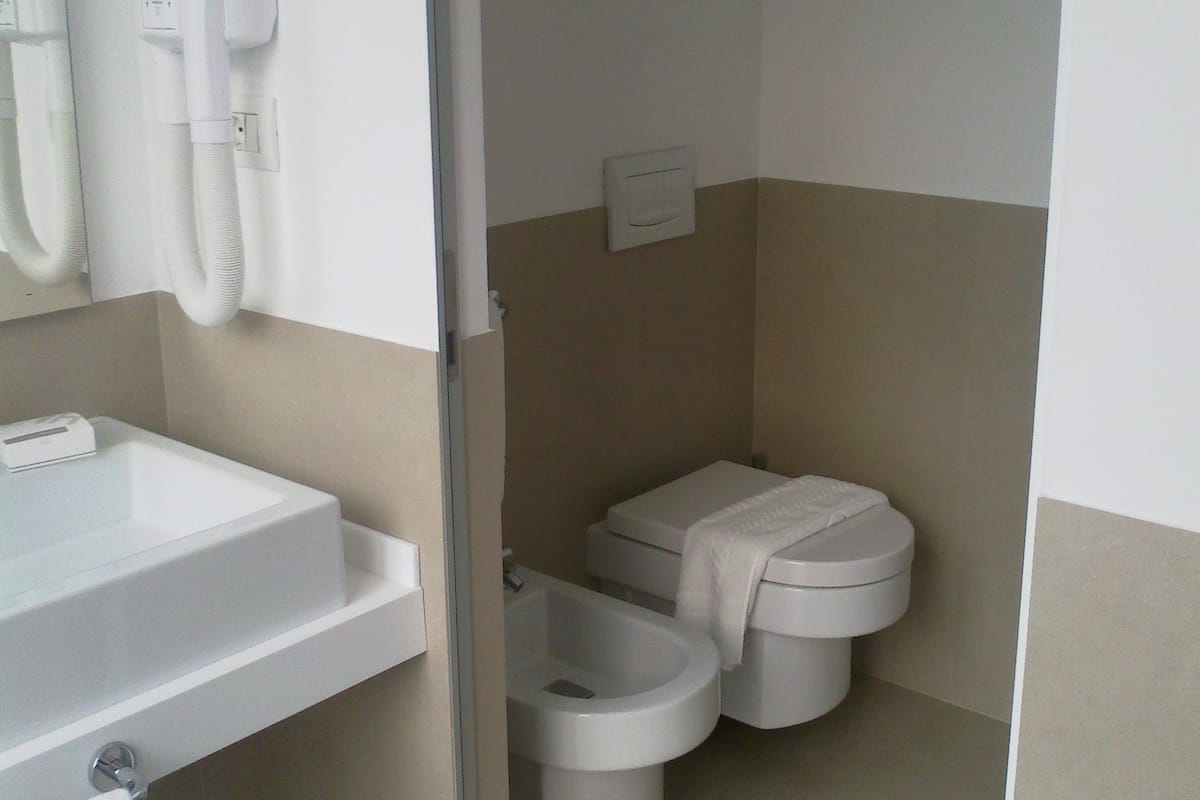 Ein Badezimmer mit einem weißen Waschbecken, einem Fön und zwei Toiletten.