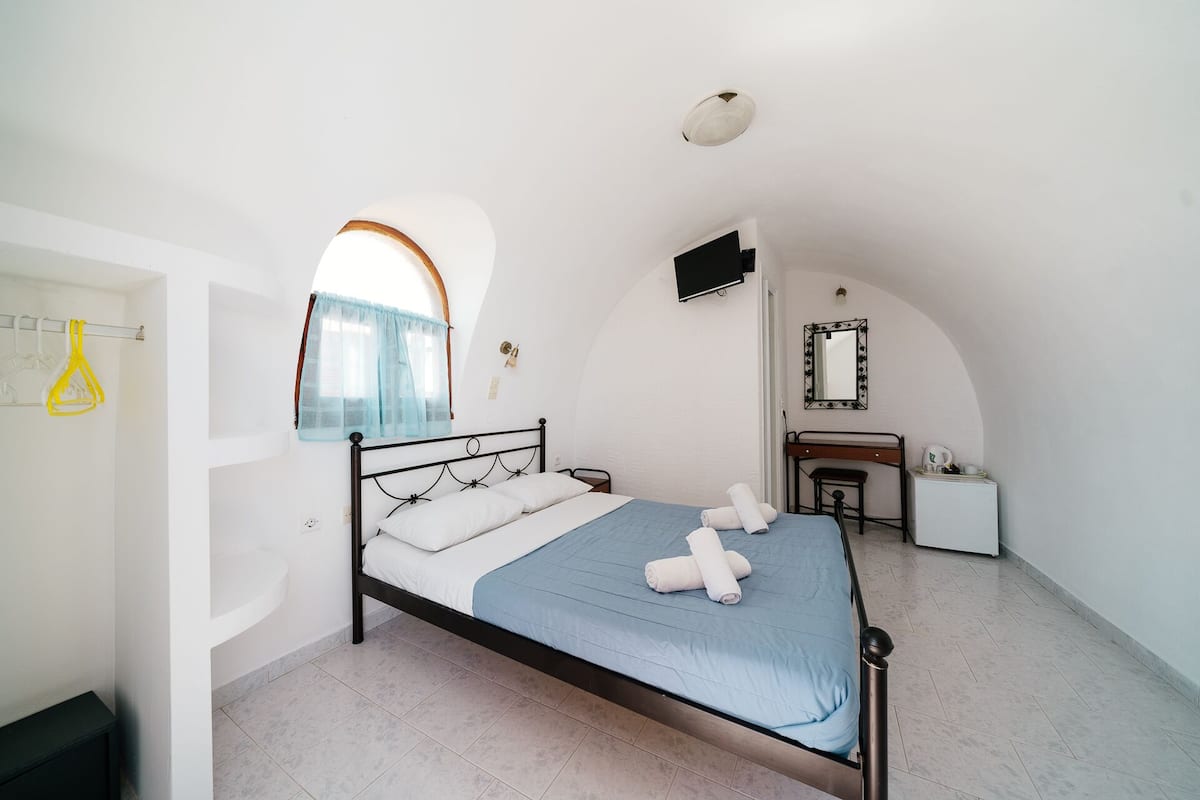 Une chambre à coucher avec un lit, un petit bureau, un miroir et une fenêtre avec un rideau.