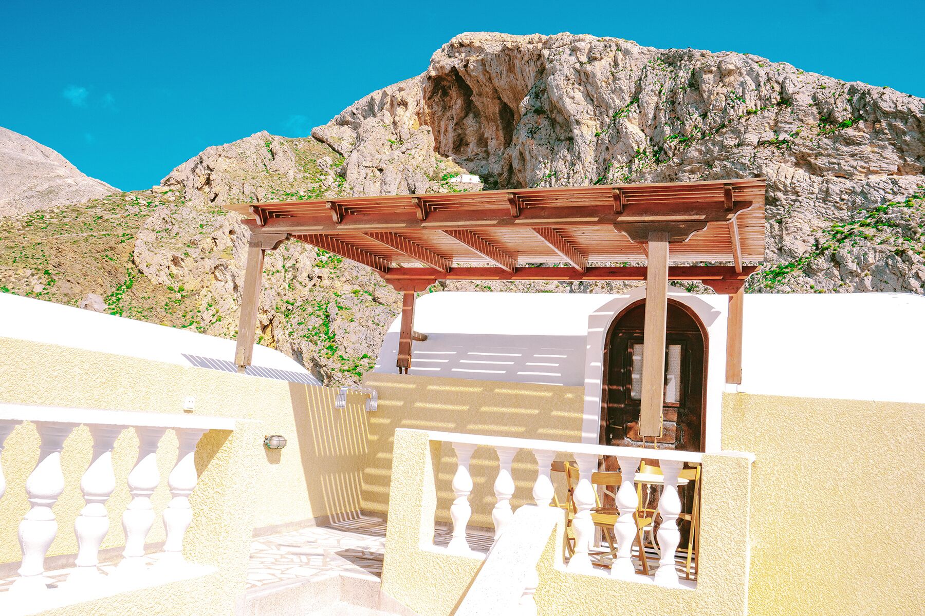 A wooden pergola structure with a white door, set against a mountainous backdrop.