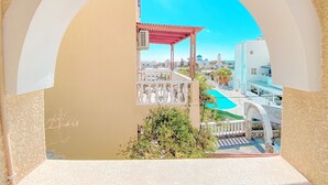 A balcony with a view of a swimming pool, a pergola, and a white fence. - Villa Dima (Santorini)