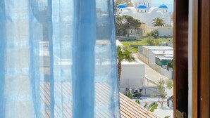A view through a window with blue curtains, revealing a building with blue domes and a clear sky. - Villa Dima (Santorini)