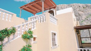 A building with a white facade, a red roofed structure, and a white balustrade. - Villa Dima (Santorini)