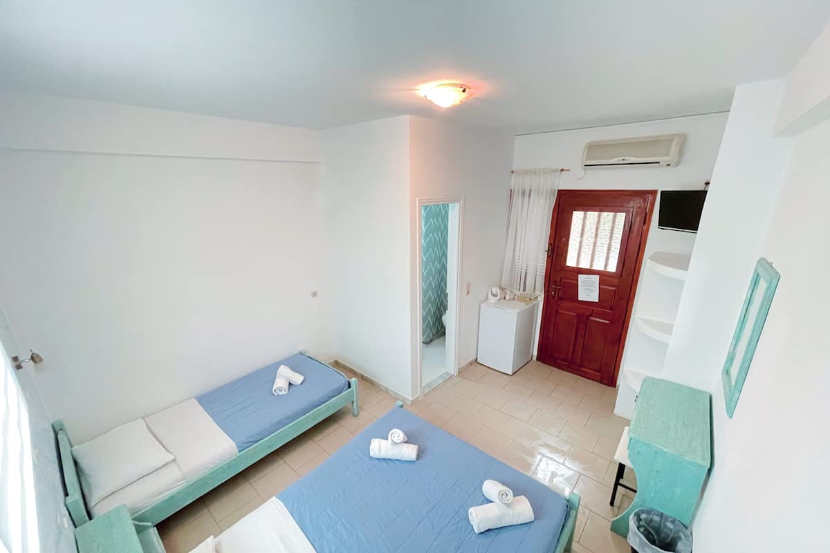 Une pièce propre et bien éclairée, avec deux lits simples, une petite table, un lave-linge et une porte donnant sur une autre pièce.