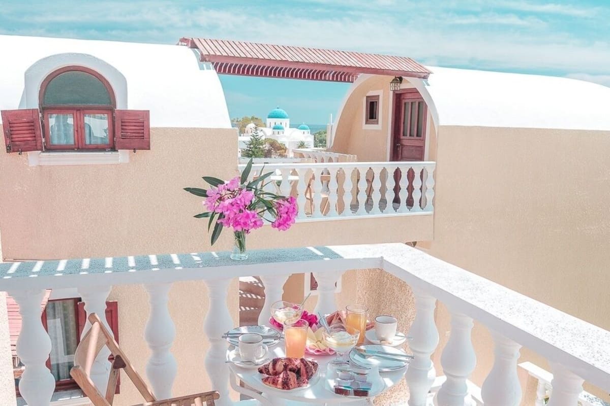 Un balcon avec une table dressée pour le petit-déjeuner, donnant sur un bâtiment à la façade blanche et aux coupoles bleues.