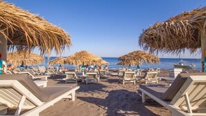 A beach with sun loungers and thatched umbrellas. - Villa Dima (Santorini)