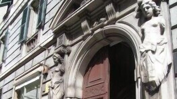 A building with a large wooden door, stone carvings, and a statue on the facade. - Hotel Suisse Genova (Genoa)