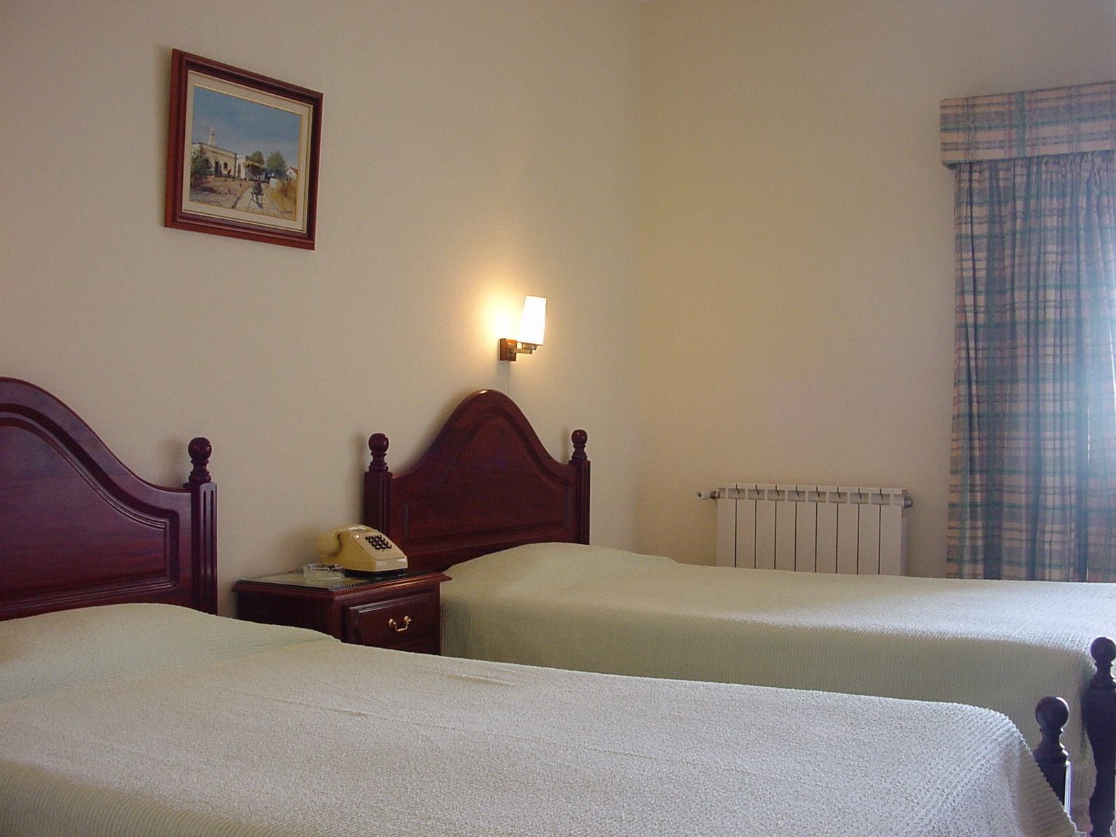 Ein Hotelzimmer mit zwei Einzelbetten, einem Nachttisch mit Telefon, einer Wandleuchte, einer Heizung und einem Bild an der Wand.