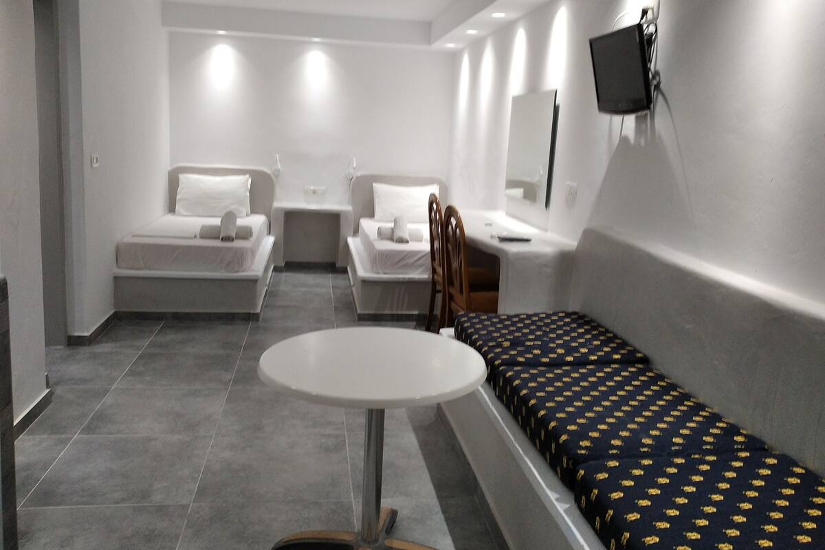 A hotel room with two single beds, a small table, a chair, and a TV mounted on the wall.