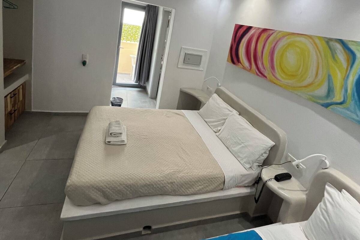 A modern hotel room with a bed, bedside table, and a colorful abstract painting on the wall.