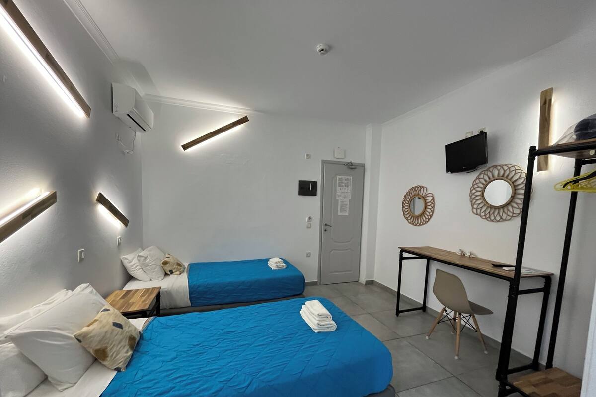 A hotel room with two beds, a desk, a chair, a TV, and a mirror.