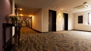A hotel corridor with a patterned carpet, wooden furniture, and a vase of flowers. - Toyo Hotel (Fukuoka)