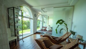 Una habitación moderna con suelo de madera, una estantería de vidrio, un banco acolchado y una planta grande.