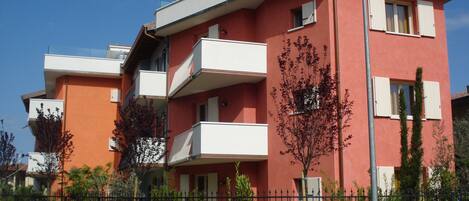 A multi-story residential building with balconies, a concrete fence, and some greenery.