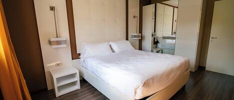 Una habitación de hotel moderna con una cama grande, una mesita de noche, un espejo y un armario.