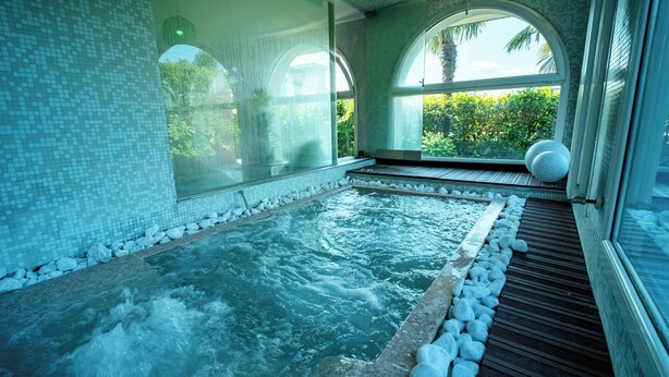 Un área de spa con jacuzzi, paredes de azulejos y ventanas arqueadas grandes.