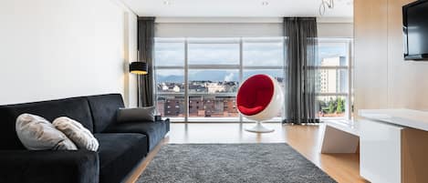 Una sala de estar moderna con un sofá negro, un sillón rojo y un ventanal con vistas a la ciudad.