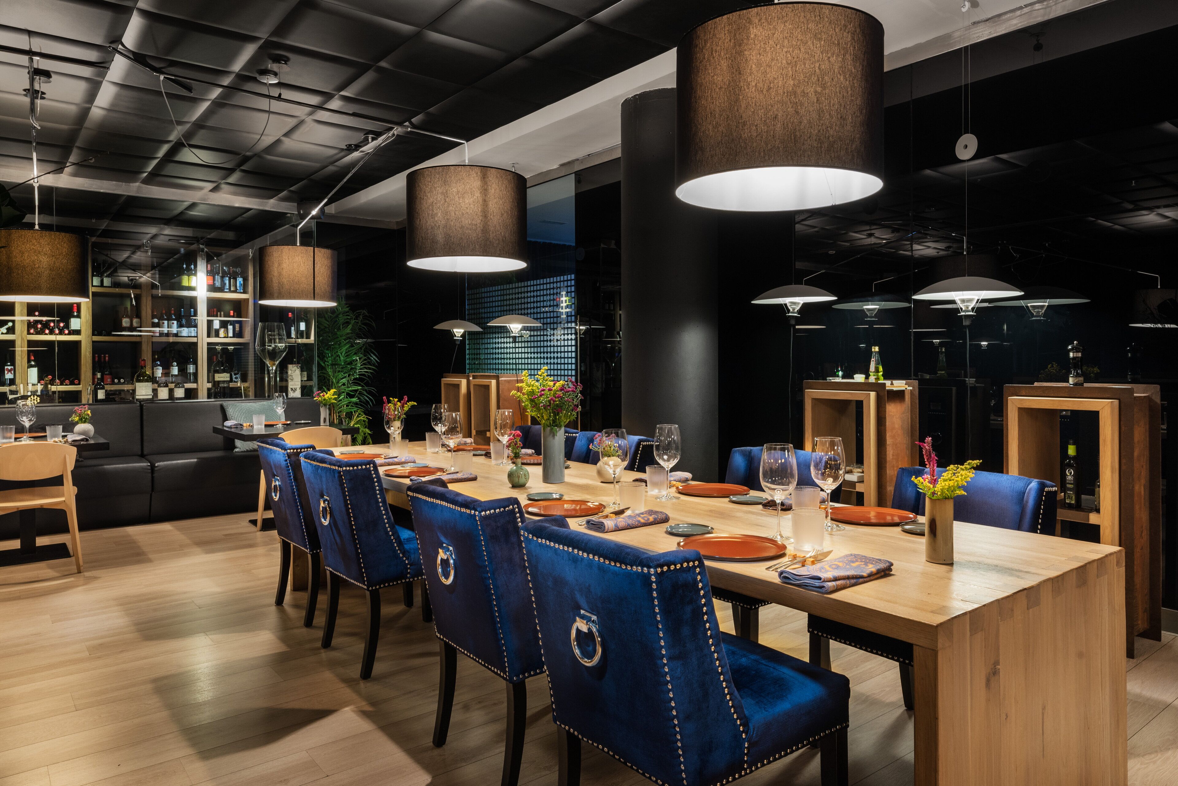 A modern dining area with a long wooden table, blue upholstered chairs, and hanging pendant lights.