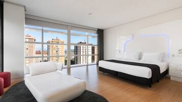 Ein modernes Hotelzimmer mit einem großen Fenster, einem Bett, einem roten Hocker und einer wandmontierten Lampe.