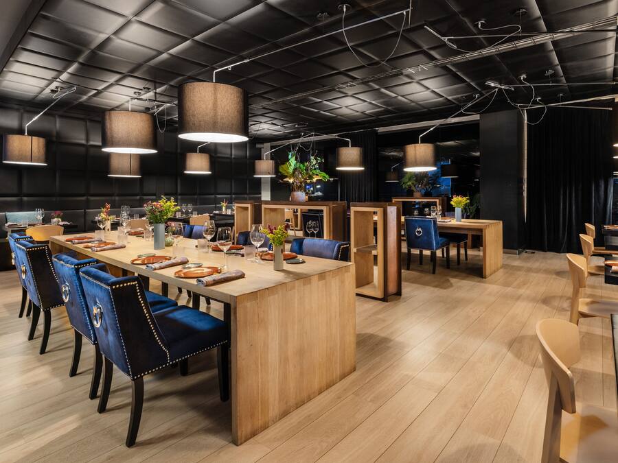 A modern restaurant with wooden tables, blue upholstered chairs, and pendant lighting.