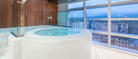 A modern indoor hot tub with a panoramic city view.