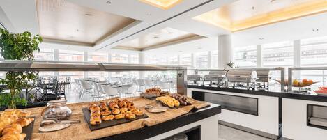 A modern breakfast buffet with pastries, a coffee station, and a view of the city.