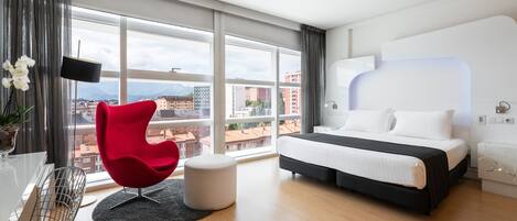 Una habitación de hotel moderna con una cama grande, una silla roja, un televisor de pantalla plana y vistas de la ciudad.