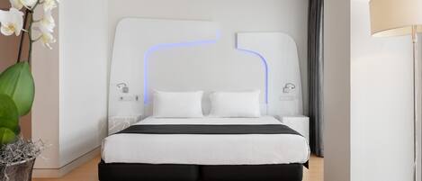A modern hotel room with a bed, bedside tables, a lamp, and a vase with flowers.