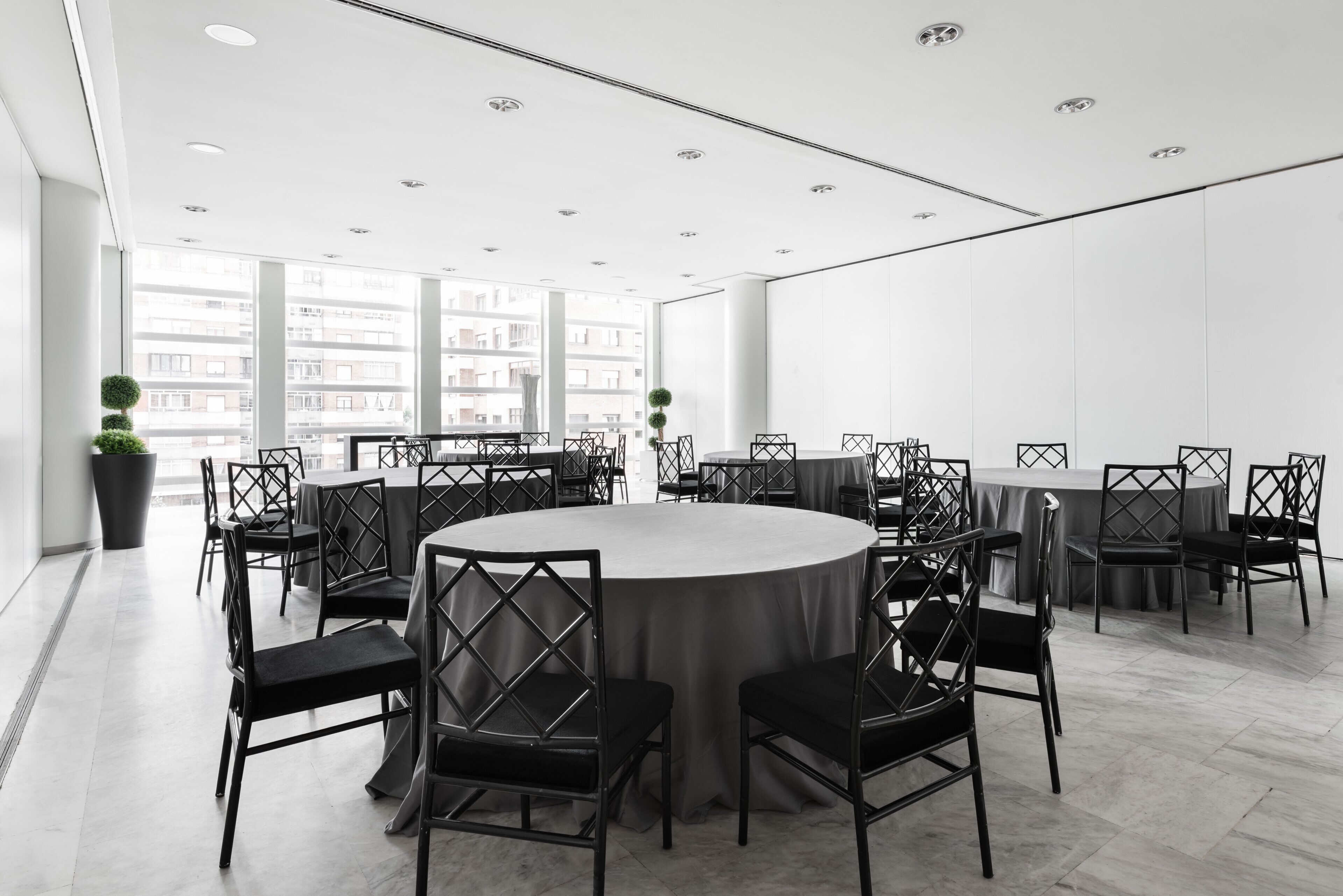 Uma sala de conferências moderna com uma mesa redonda cercada por cadeiras, grandes janelas e vista para a cidade.