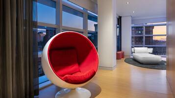 Een modern interieur met een rode eierstoel, een witte bank en een uitzicht op gebouwen door grote ramen.