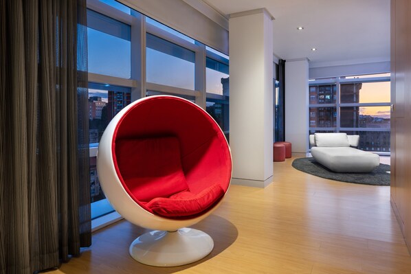 A modern interior with a red egg chair, a white sofa, and a view of buildings through large windows. - Eurostars Palacio de Cristal (Oviedo)