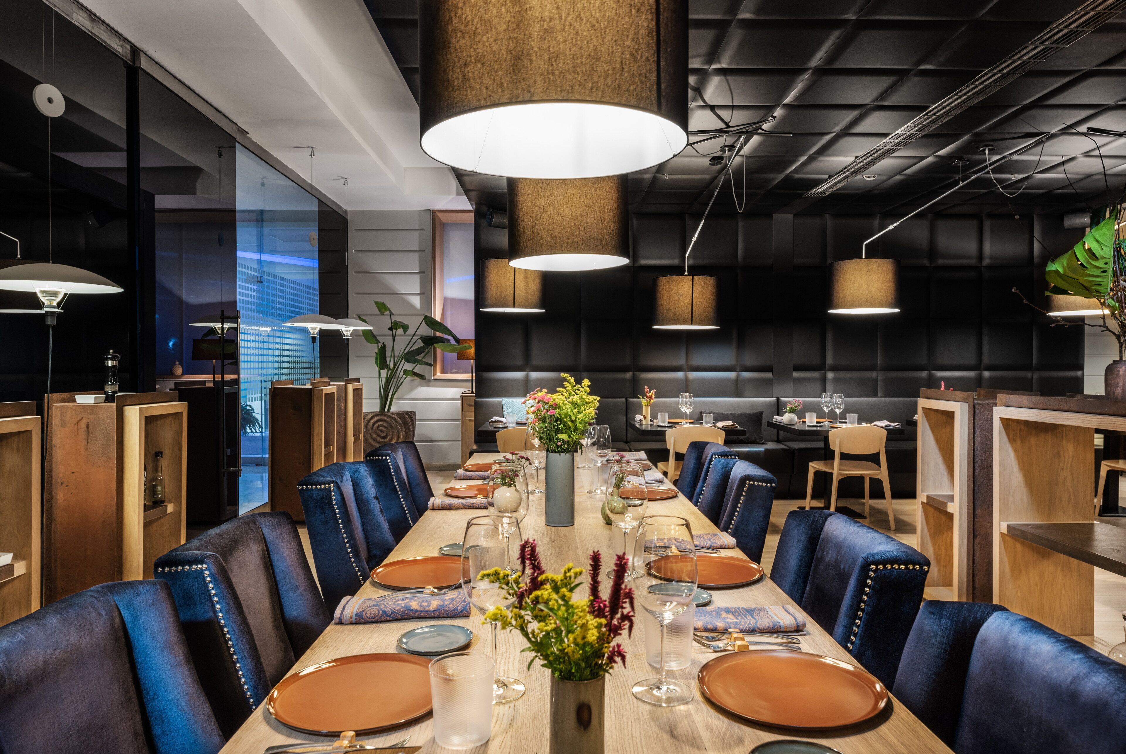 A modern dining area with a long wooden table, blue upholstered chairs, and pendant lighting.
