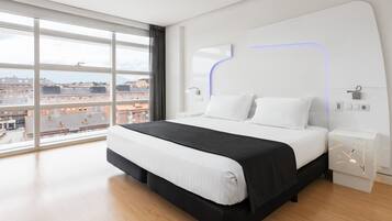 A modern hotel room with a large bed, a view of the city, and a minimalist design.