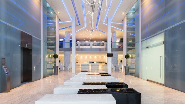 Rebedor d'hotel modern amb una zona d'estar central, parets de vidre i un pis superior.