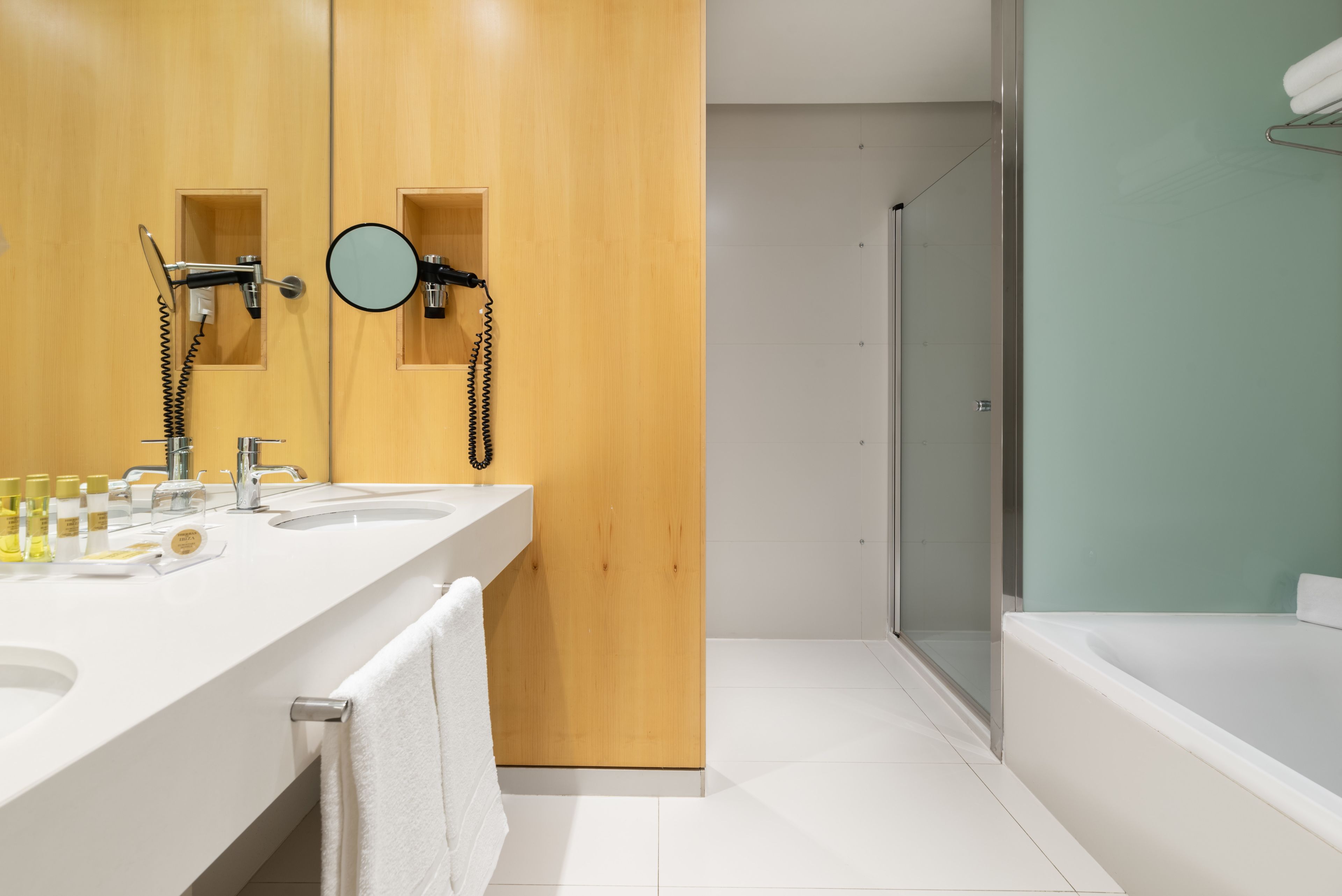 Un baño moderno con un mueble de tocador de madera, una cabina de ducha de vidrio y una bañera blanca.