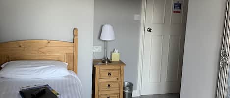 Habitación de hotel con cabecera de madera, dos camas, lámpara de noche, mesita de noche, cubo de basura, puerta con un letrero y un espejo.