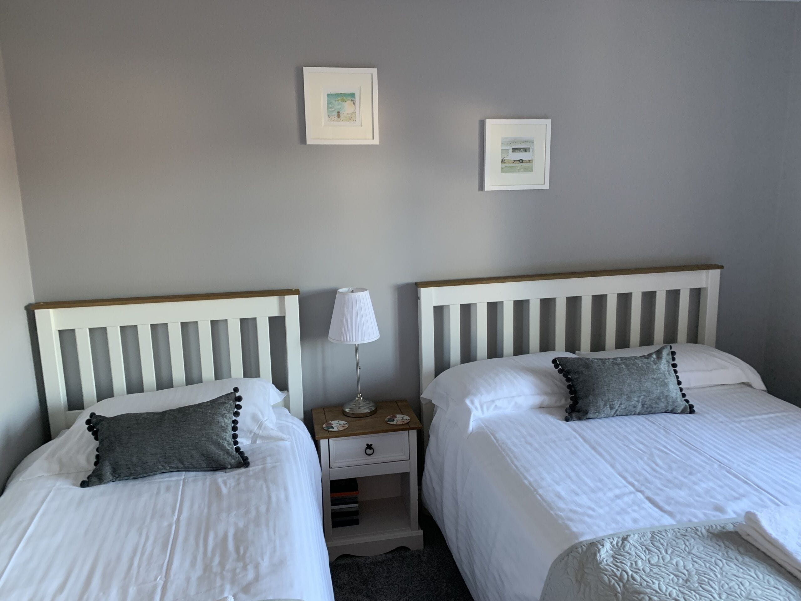Ein Schlafzimmer mit zwei Einzelbetten, einem Nachttisch mit Lampe und zwei gerahmten Bildern an der Wand.