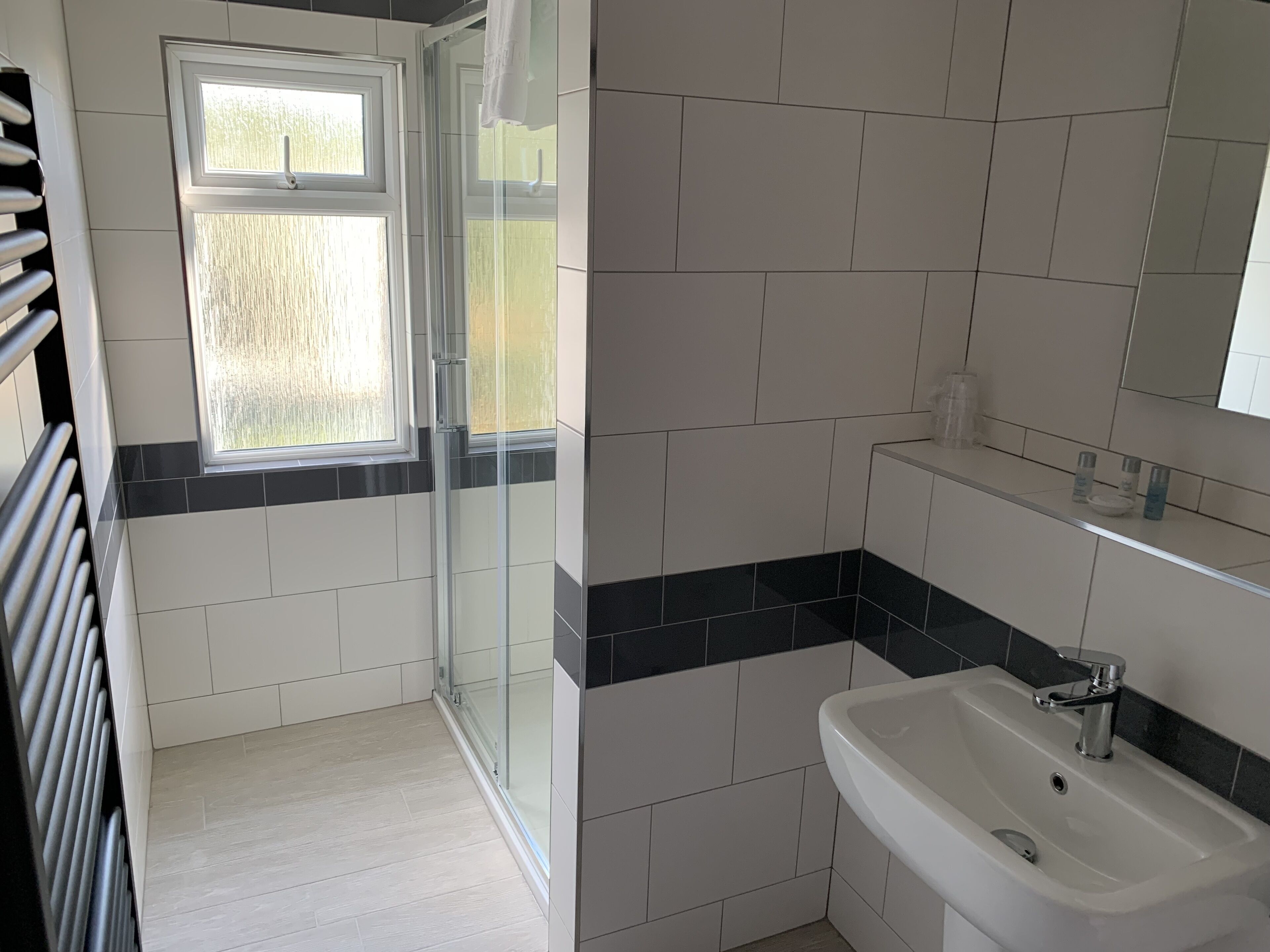 A bathroom with a glass shower enclosure, a sink with a mirror above, and a window providing natural light.