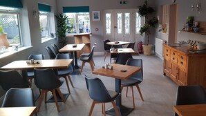 A dining area with multiple tables and chairs, a wooden cabinet, and a potted plant. - Hensleigh House (Bridport)
