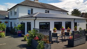 A two-story white building with a grey roof, large windows, and a patio area with outdoor seating. - Hensleigh House (Bridport)
