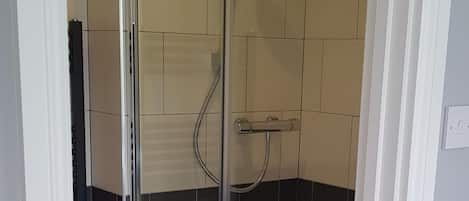 Ducha con paredes de vidrio, una toalla colgada en el picaporte y pisos de madera.