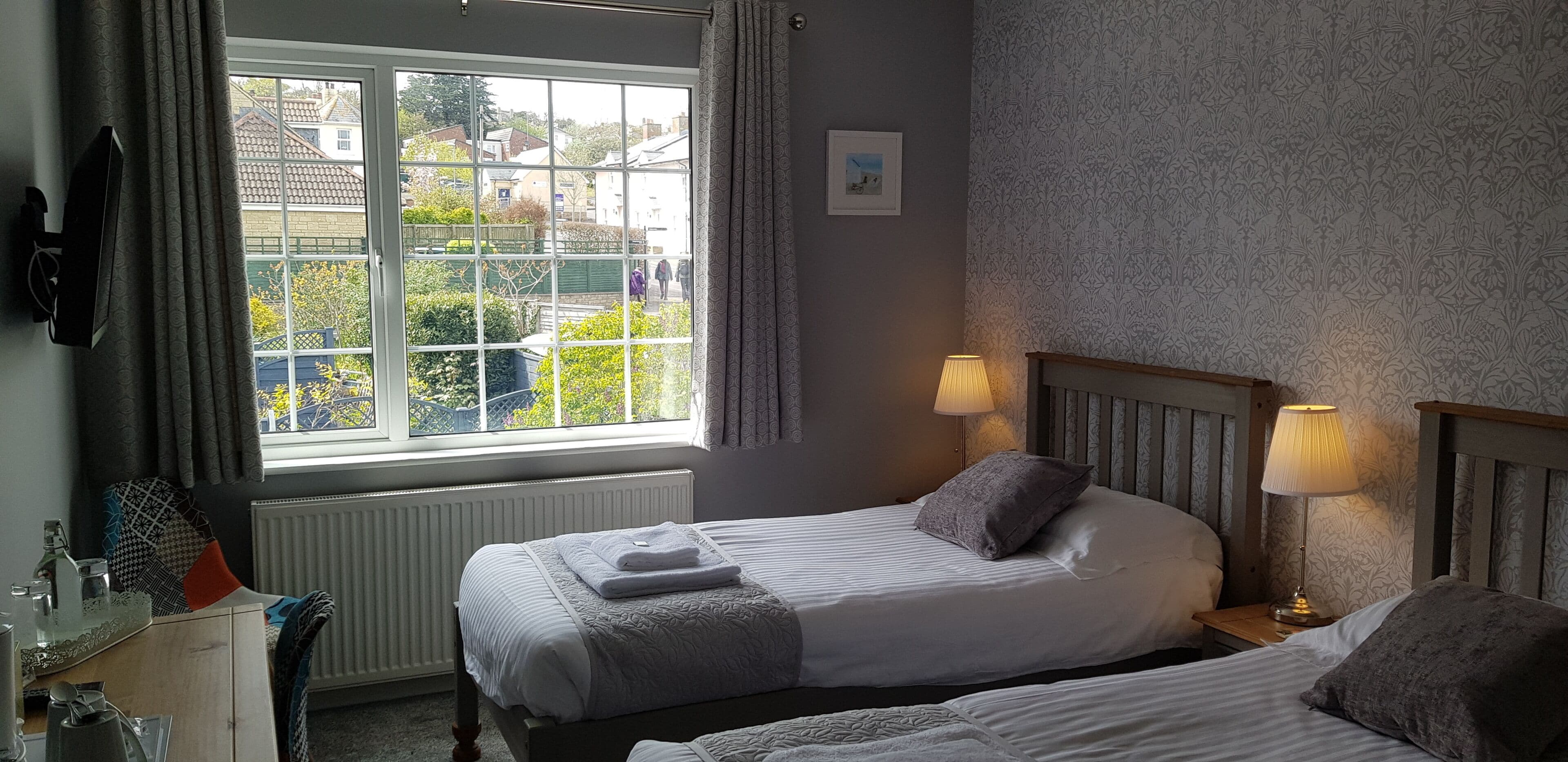 Une chambre avec deux lits, une fenêtre donnant sur l’extérieur, une lampe de chevet et un radiateur.